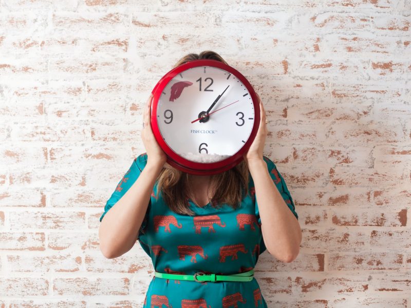 woman covering face using wall clock